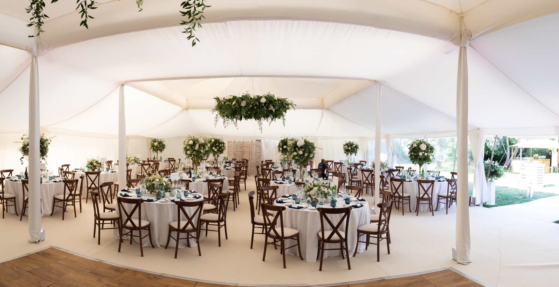 A white wedding table layout on a black floor with dark wood cross back chairs and dark green glases and napkins