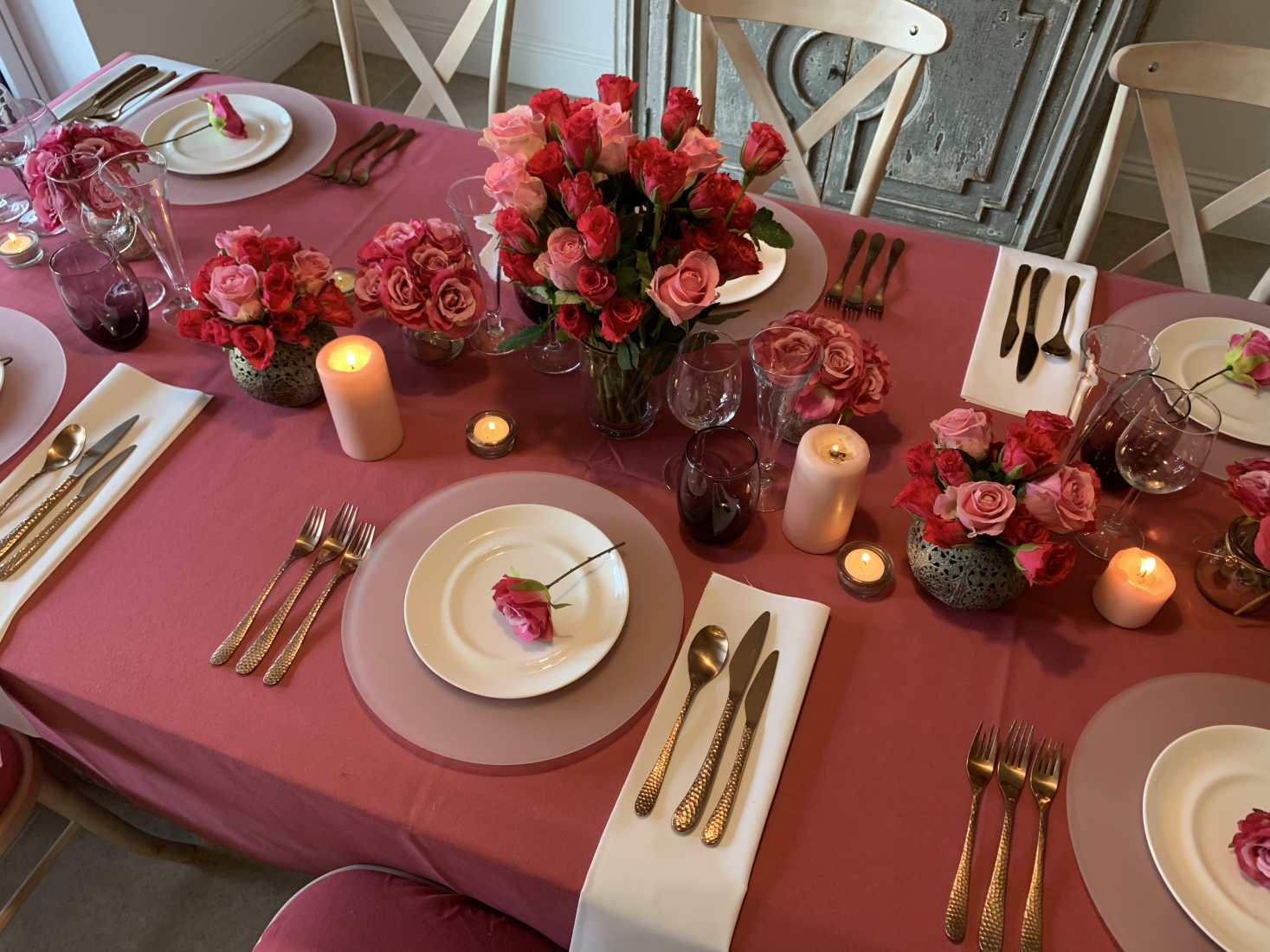 A beautifully laid table for a Valentine's dinner at home, with fancy crockery and glasses, best cutlery, candles and lots of red roses in different pots.