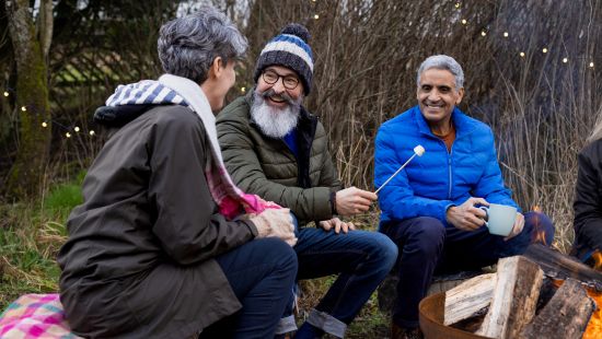Two men and a woman on outddor clothing toasting marshmallows 