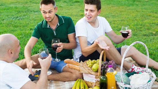 Three guys in casual summer clothes sitting on the grass at a company picnic
