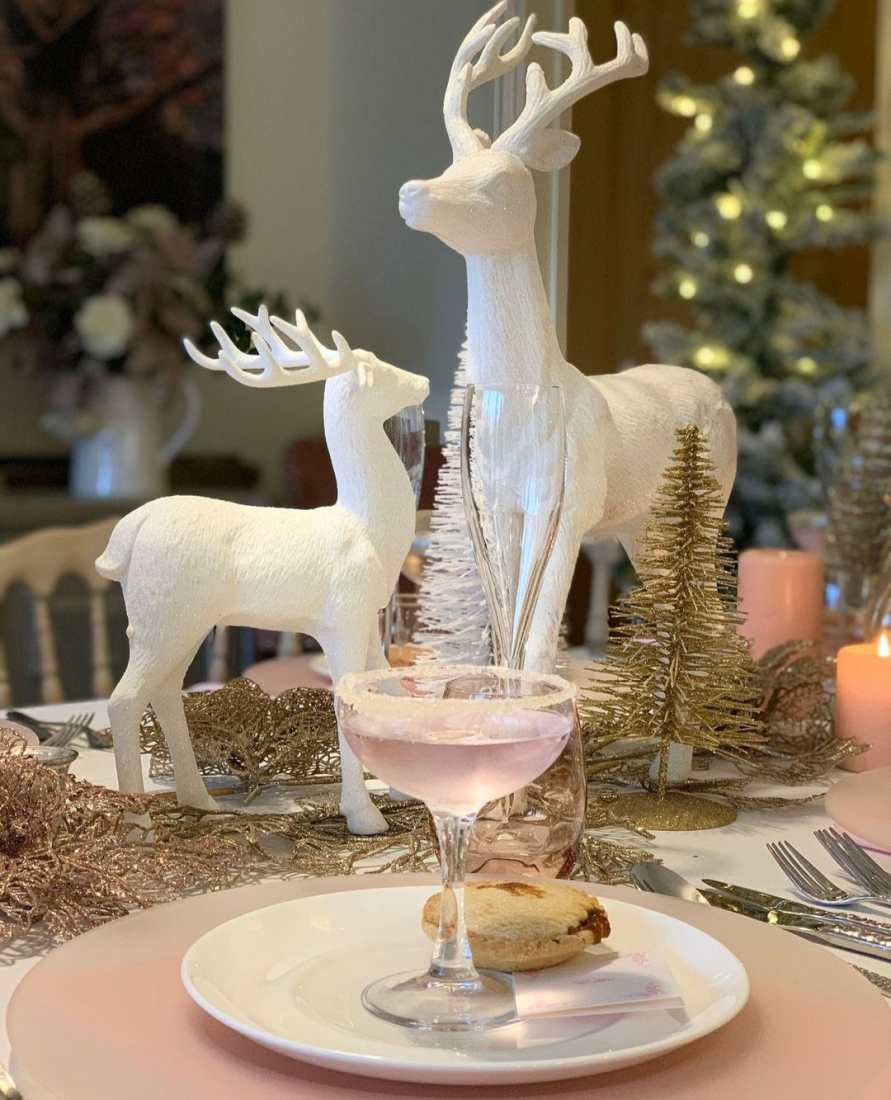 White reindeer table centrepieces, and a white plate with a mince pie and rosé fizz in a champagne saucer, in a Sugar Plum Cafe theme.