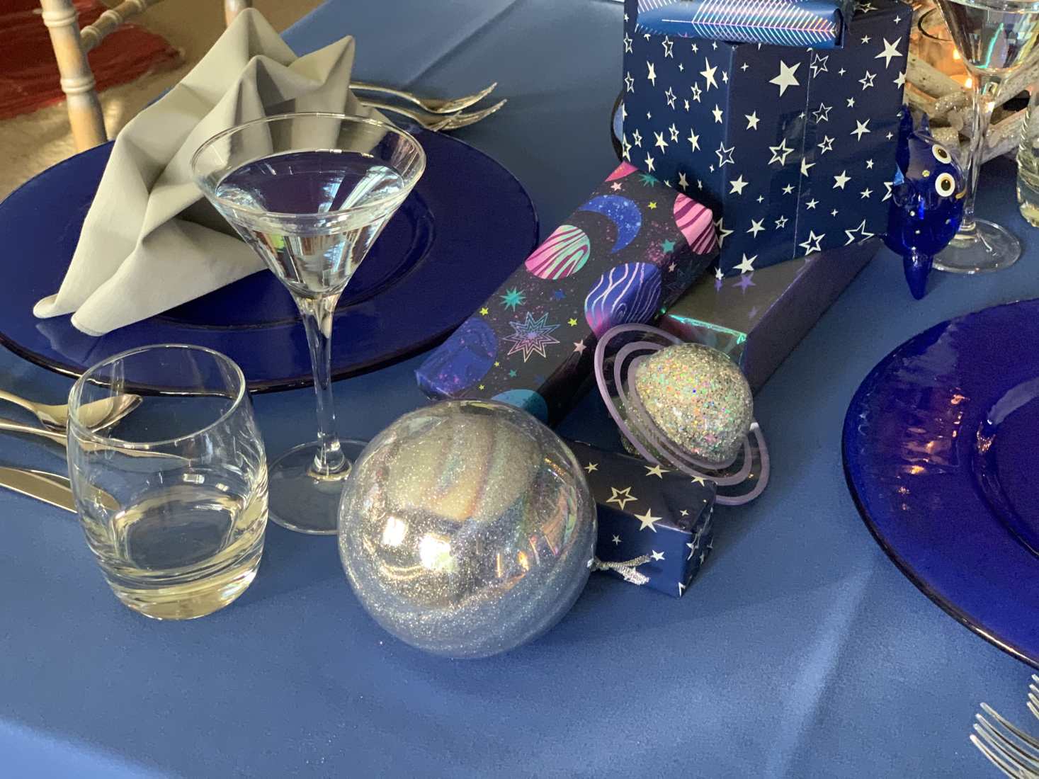 Blue Beyond styled Christmas place setting with blue tablecloth and crockery, grey star-shaped napkins, plus presents and table ornaments with space designs
