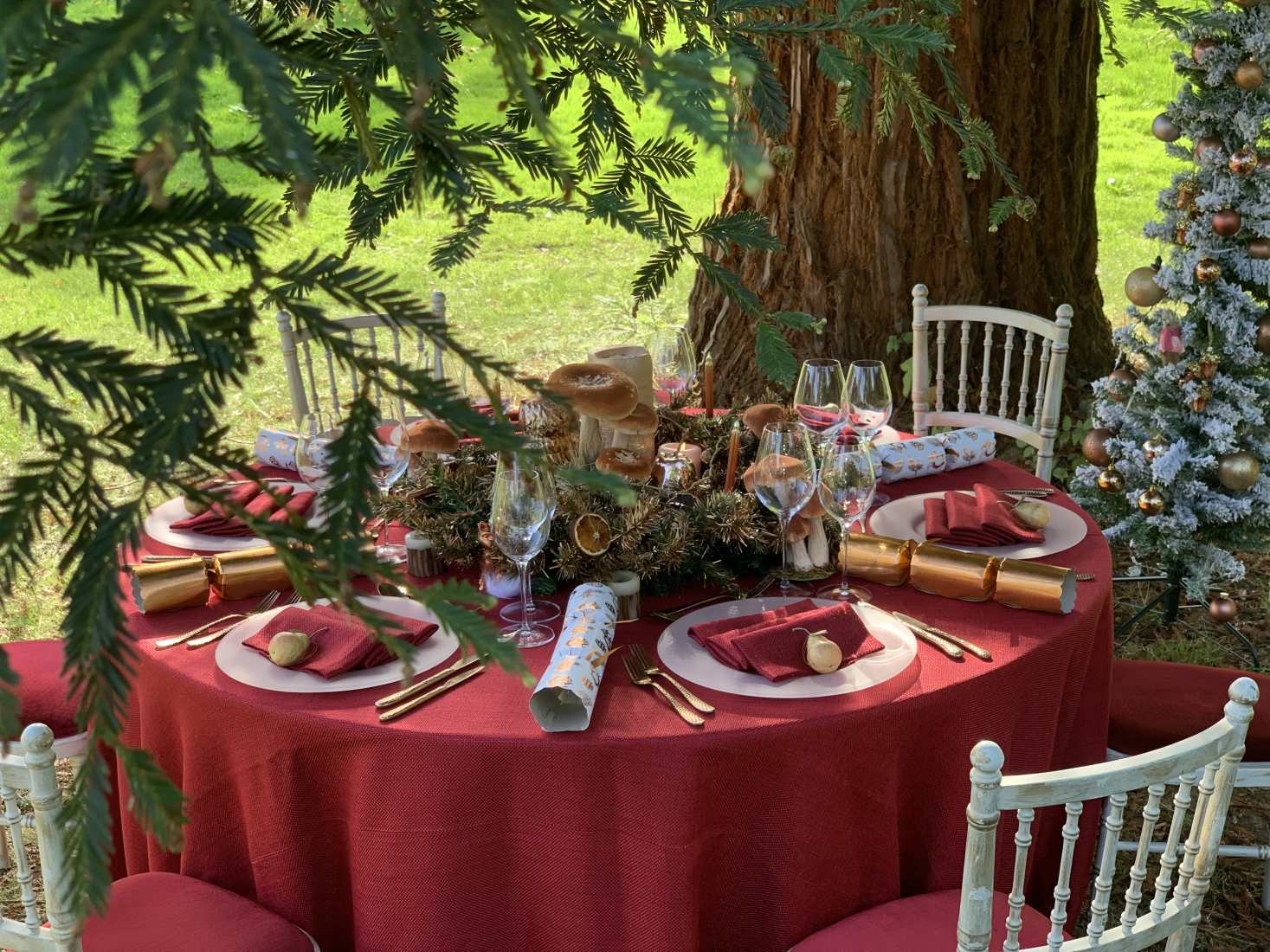 Copper Country Christmas styled table with red tablecloth, napkins, and rose gold cutlery, in an outdoor winter forest setting.