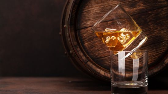Two glasses of whisky on the rocks next to a barrel.