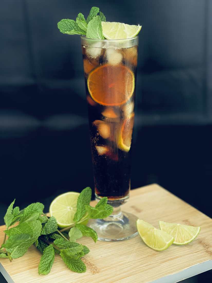 A Long Island Iced Tea cocktail served with a lemon wedge and sprigs of mint.
