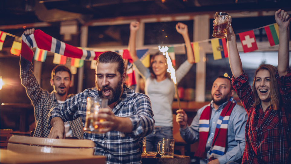 Excited group of cheering people with football scarves and flags at a corporate sports screening event.