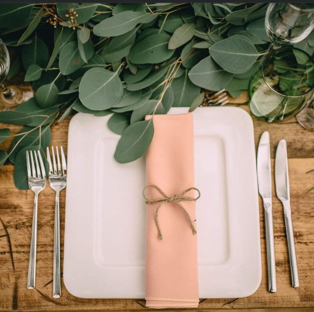 A peach and white table setting for a wedding, with plate, napkin, cutlery, and lots of eucalyptus.