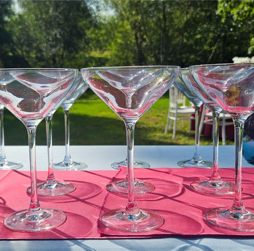 Rows of Martini glasses on a pink table runner at an outdoor event.