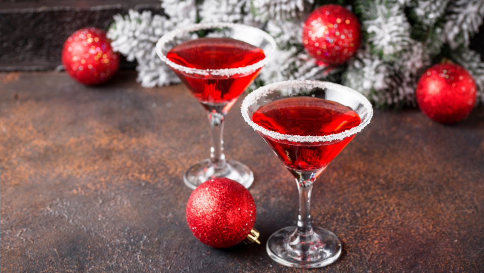 Two red Christmas cocktails in martini glasses with a red glittery bauble against a white Christmas tree.