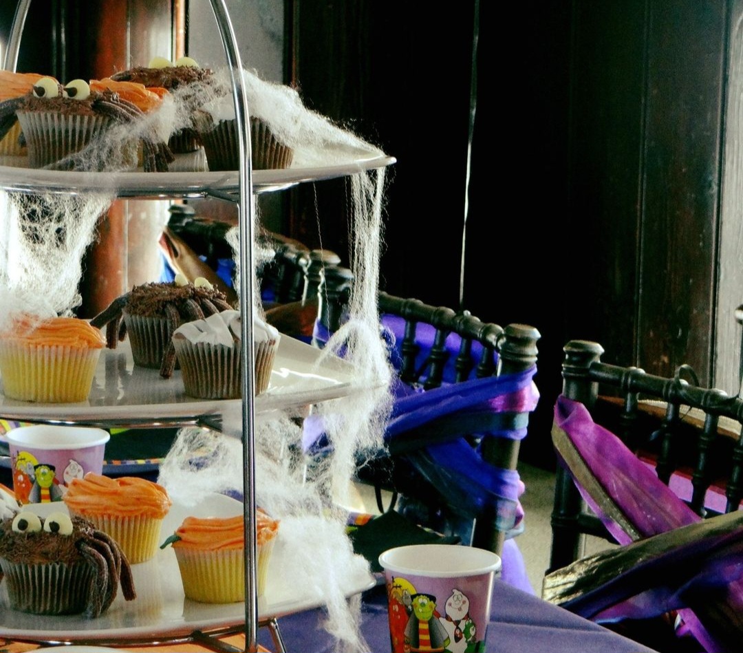 A cobweb-draped afternoon tea stand on a Halloween themed table for corporate Halloween events.