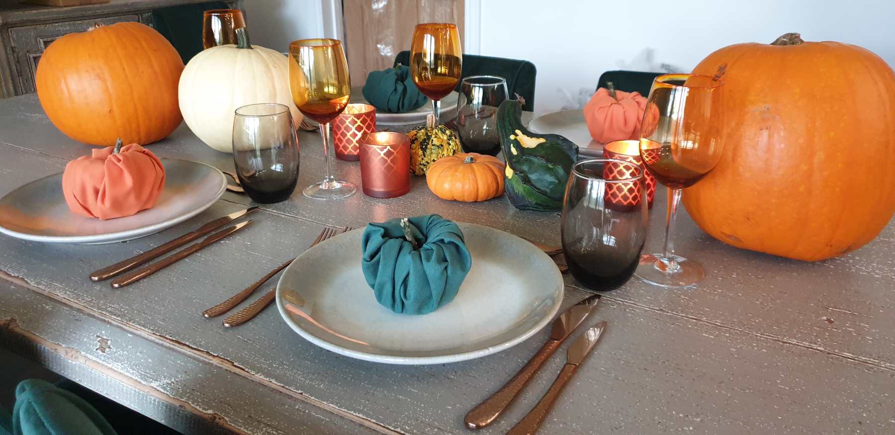 A Halloween table with pumpkins, candles, coloured glassware and napkins shaped into pumpkins.