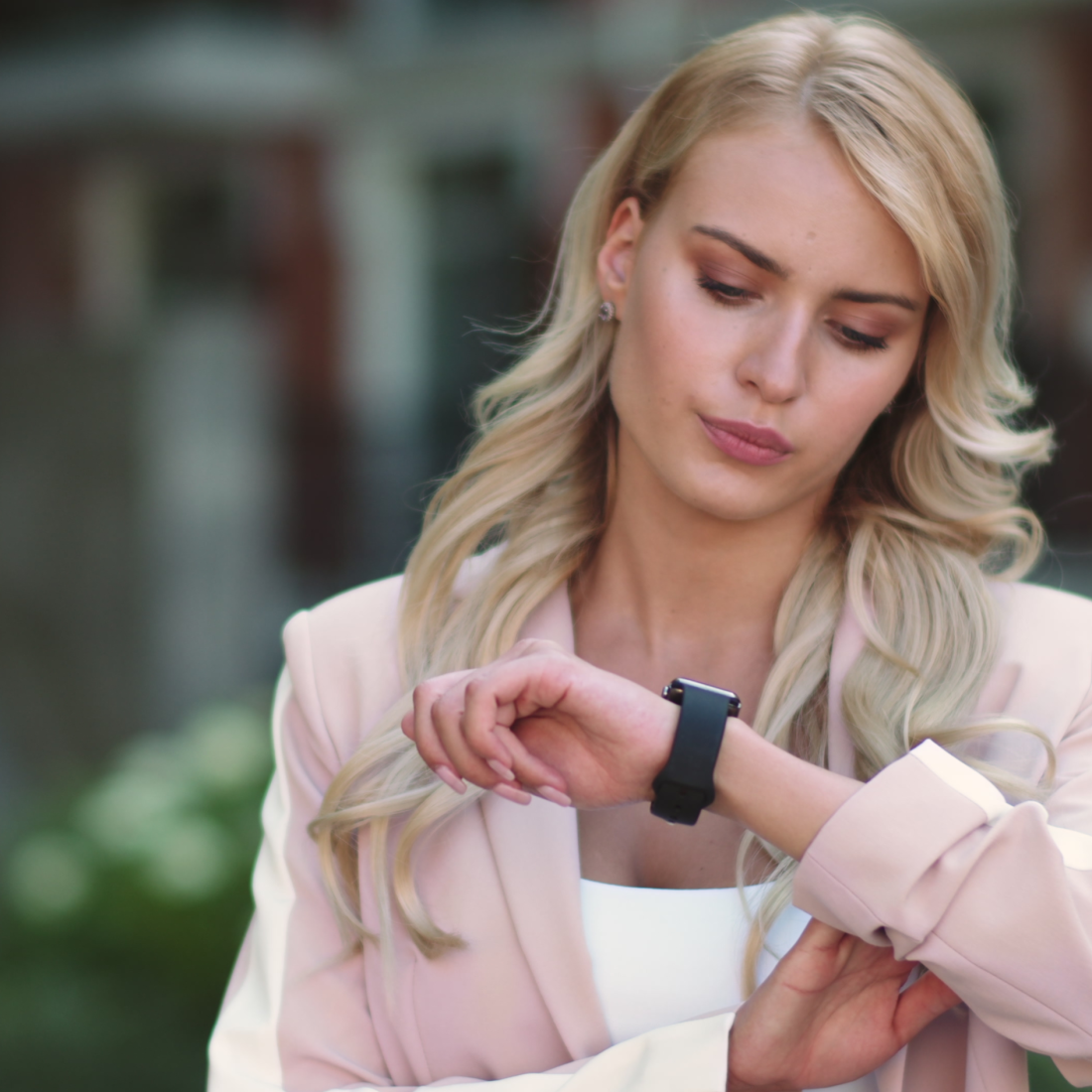 A pretty blonde woman in a beige jacket looking at her watch.