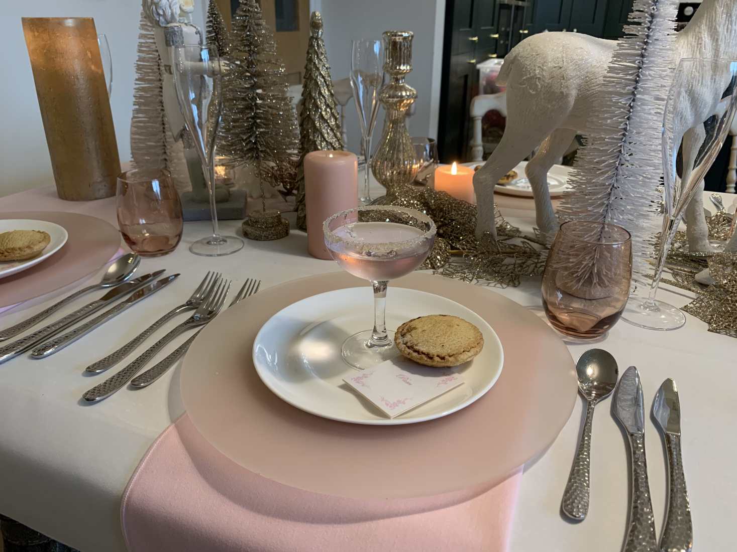 A sugar plum Christmas table setting, with rose pink napkins and chargers, a white plate with a mince pie and filled champage saucer.