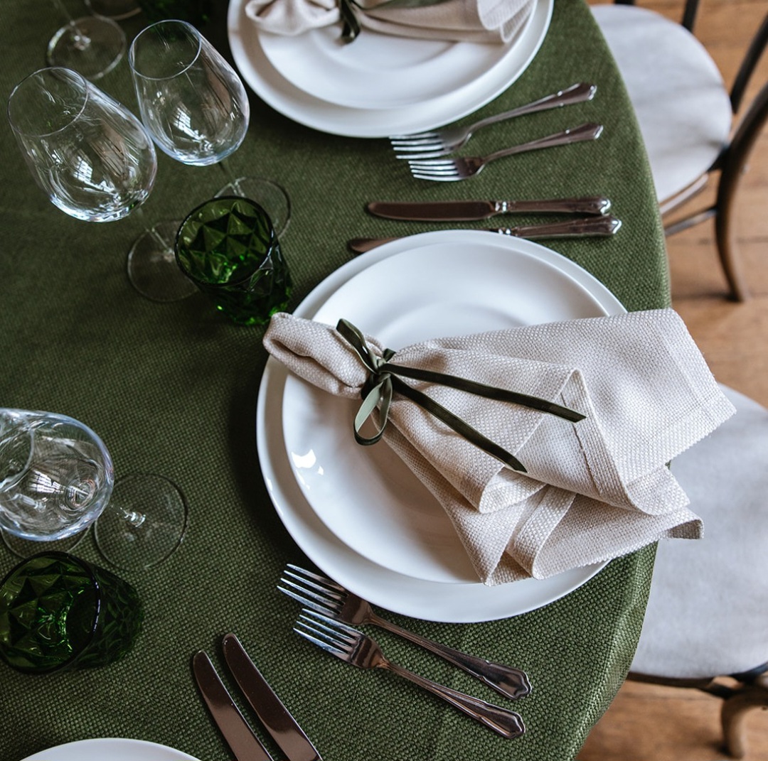 An olive green Easter table, with coloured line table cloth, napkins, white plates, silver cutlery and crystal wine glasses.