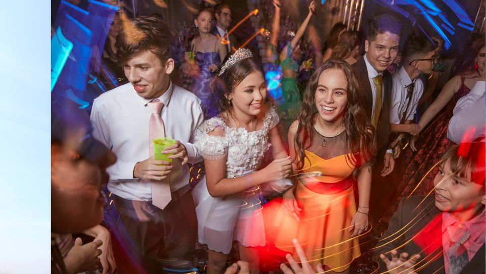 A group of dressed up teend dancing and smiling at their school prom.