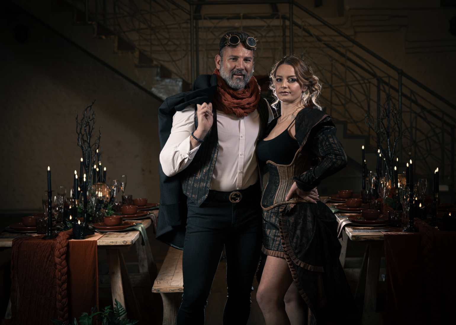 A couple dressed in steampunk outfits stand infront of a table laid up for a steampunk themed wedding breakfast