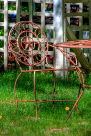 One metal chair and table in garden in front of white lattice fence