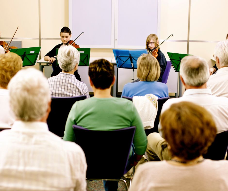 Rows of adults watching two young violinists at a school concert