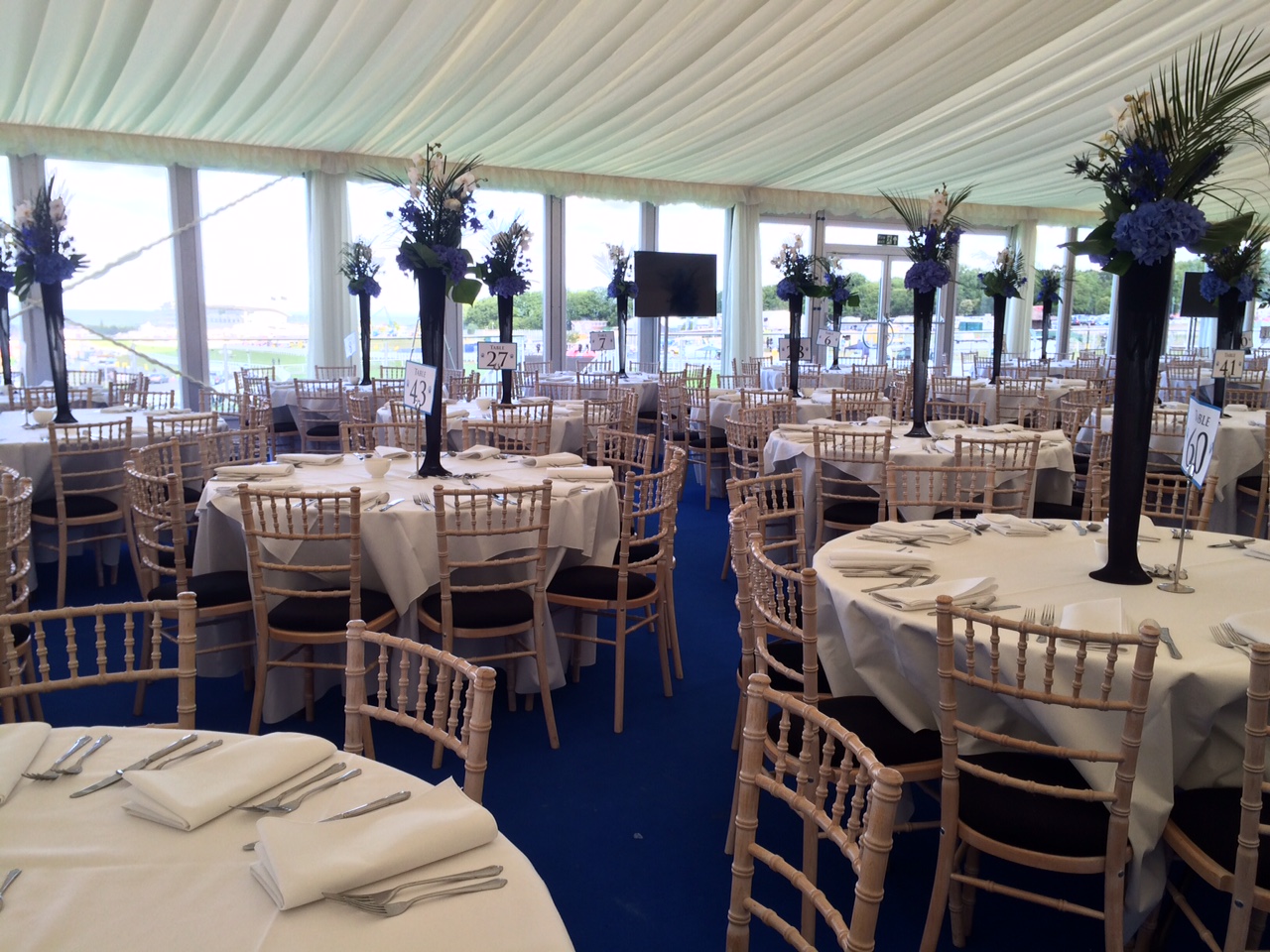 A white wedding table layout on a blue carpet with statement navy blue tall vases of flowers.