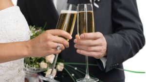 A bride and groom at a white wedding clinking champage glasses.
