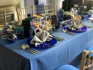 Blue Beyond styled Christmas table with blue tablecloth and crockery, grey star-shaped napkins, plus presents and table ornaments with space designs