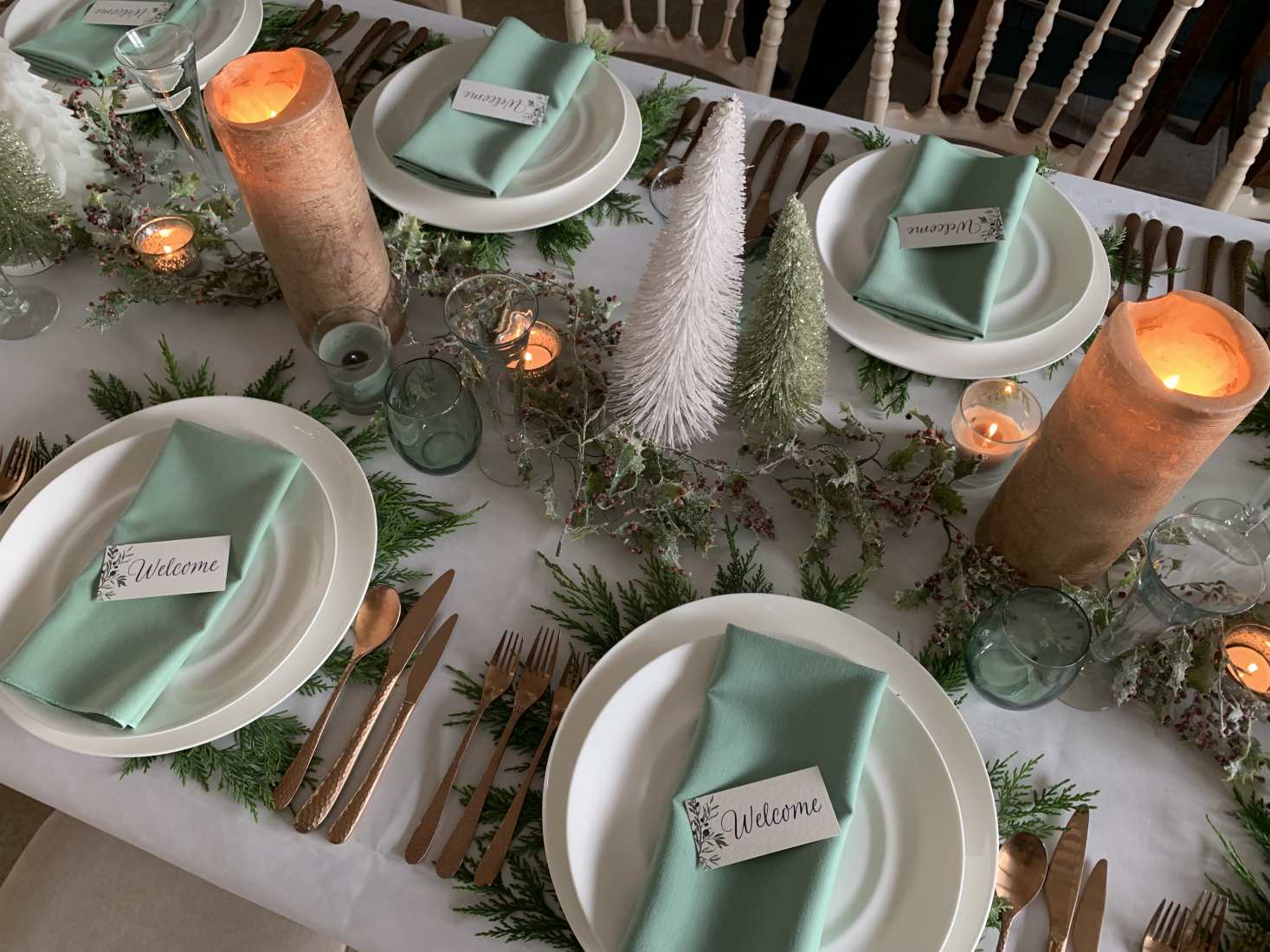 Christmas party table settings in a white, peach and Celadon green theme, with white crockery and rose gold cutlery.