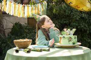 A girl sits at a table, dressed in green with a green themed birthday cake