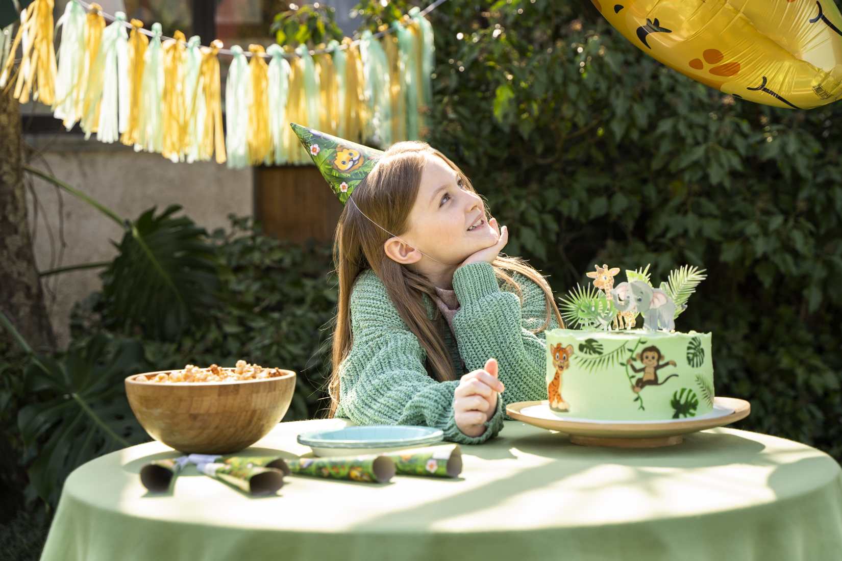 A girl sits at a table, dressed in green with a green themed birthday cake